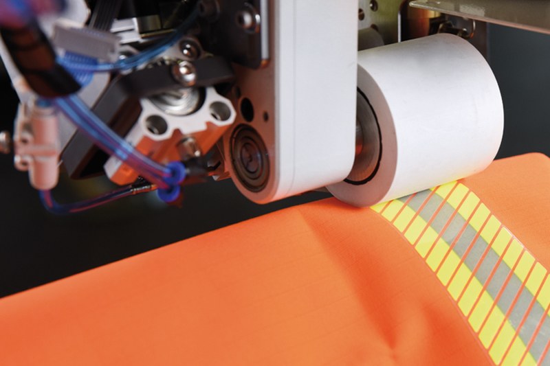 PFAFF 8323 aplicando cinta reflectante sobre una prenda de alta visibilidad naranja